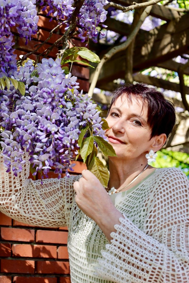 Frau mit Glyzinienblüten an einer Backsteinmauer