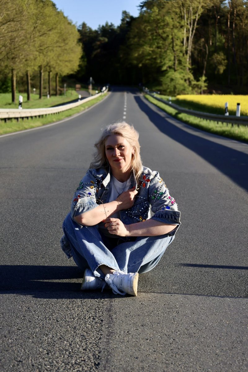 Frau sitzt auf einer leeren Allee im Sonnenlicht