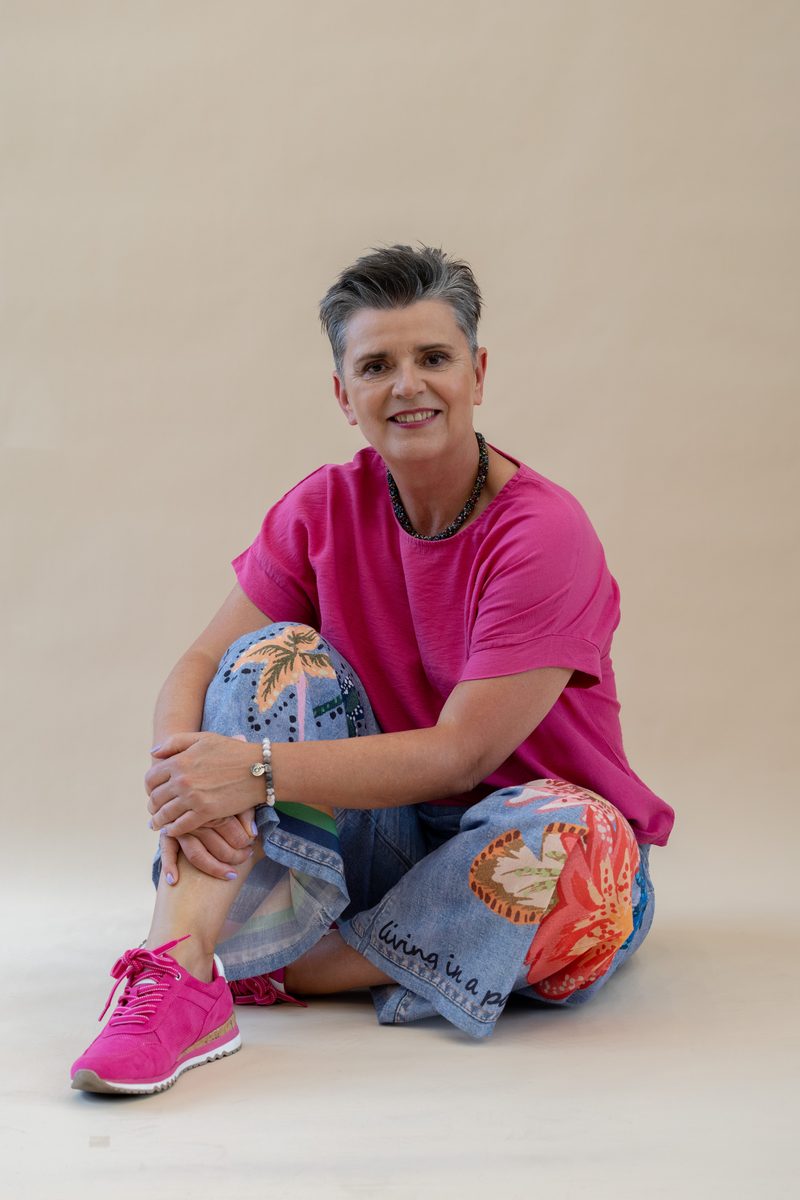 Sitzendes Portrait in pinkem Shirt und bemalter Jeans