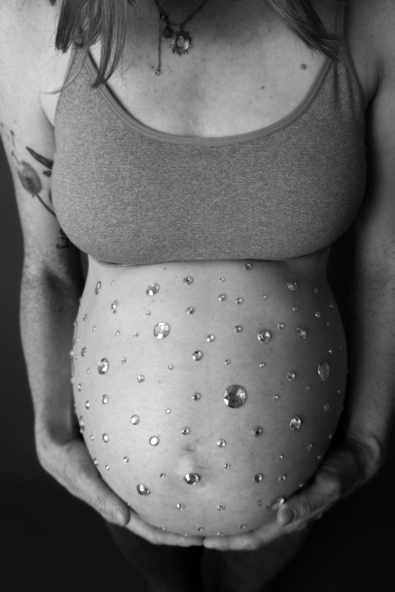 Babybauch mit aufgeklebten Glitzersteinen verziert, Nahaufnahme in schwarzweiß