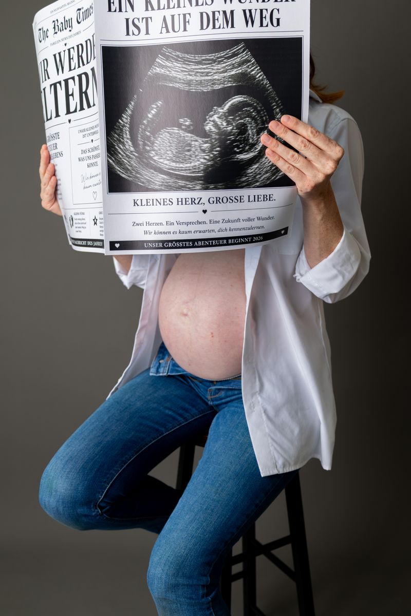 Schwangere Frau liest eine Zeitung mit Ultraschallbild, Babybauch sichtbar