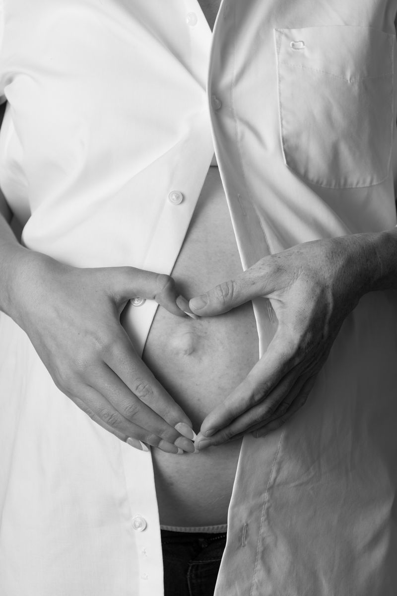 Zwei Hände formen ein Herz auf dem Babybauch, Nahaufnahme in schwarzweiß