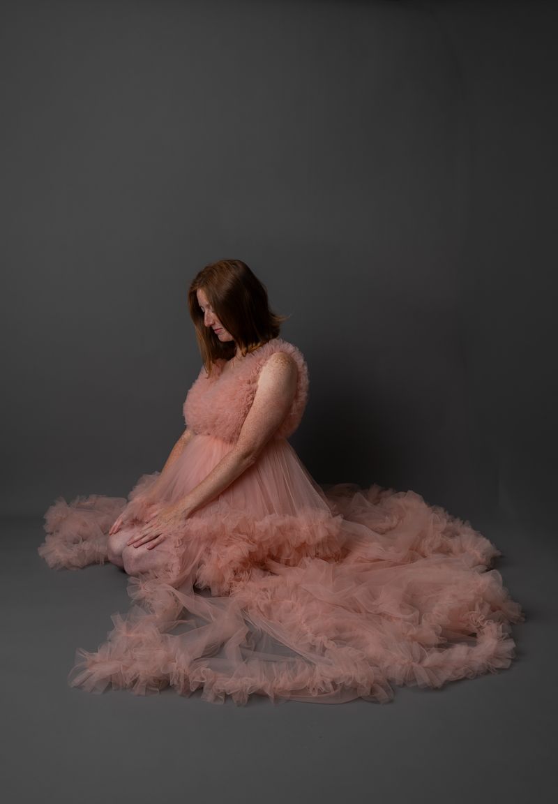 Schwangere Frau im rosa Tüllkleid, kniend im Studio