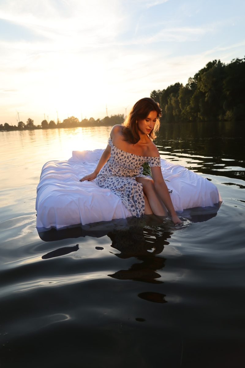 Frau im Sommerkleid auf dem Wasser bei Sonnenuntergang
